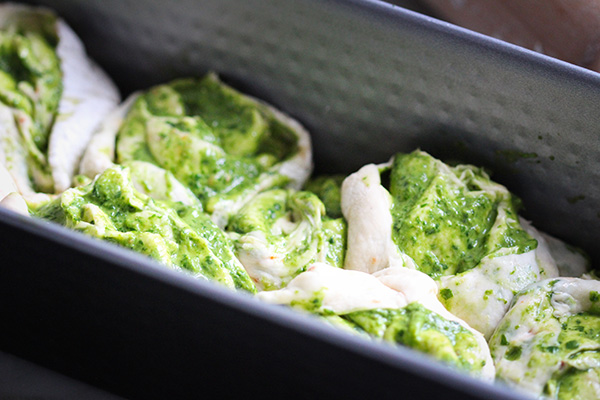 Teig für das Partyzupfbrot gefüllt mit Pesto in die Form schichten.